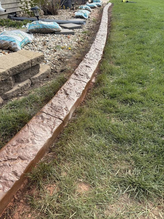 Long stamped brown concrete curb following a sweeping landscape bed.