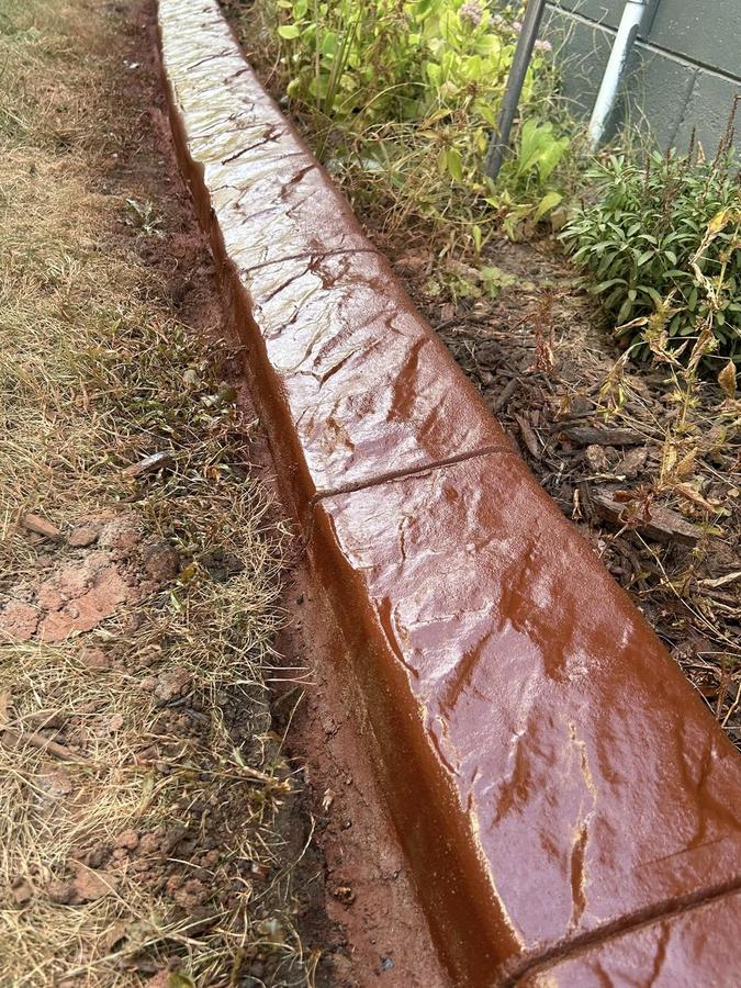 Red stamped concrete curbing installed as a polished lawn and bed border.