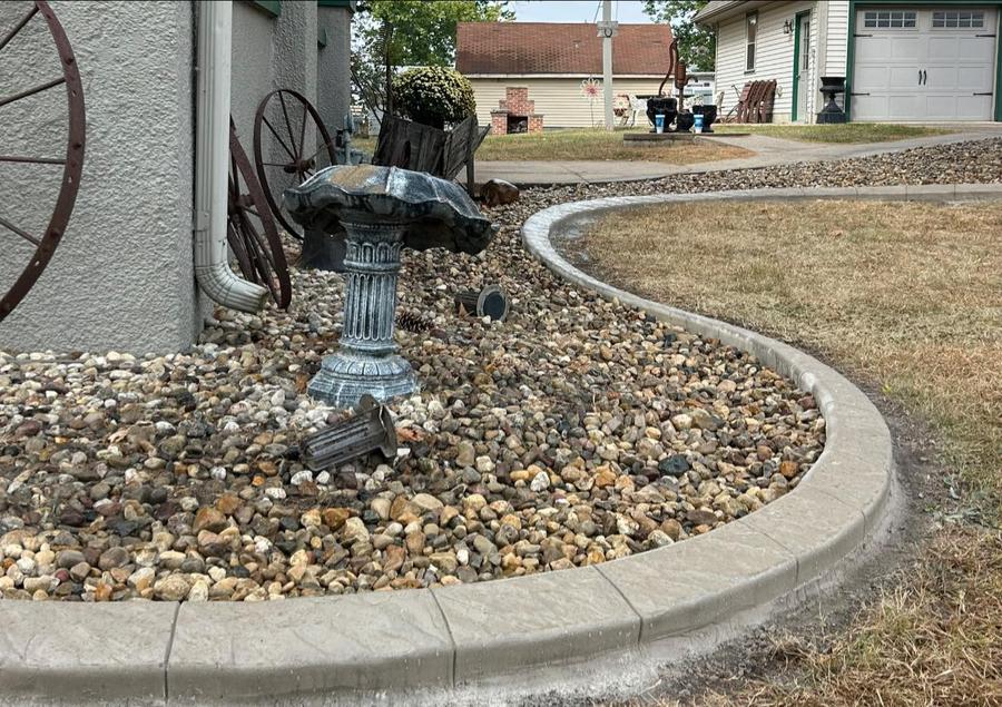 Concrete curb edging around river rock and landscaping near a home.